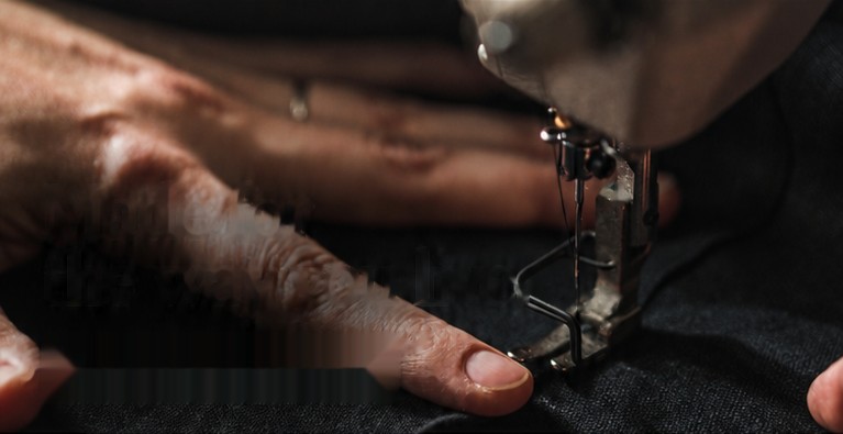 Hands guiding cloth under a sewing machine